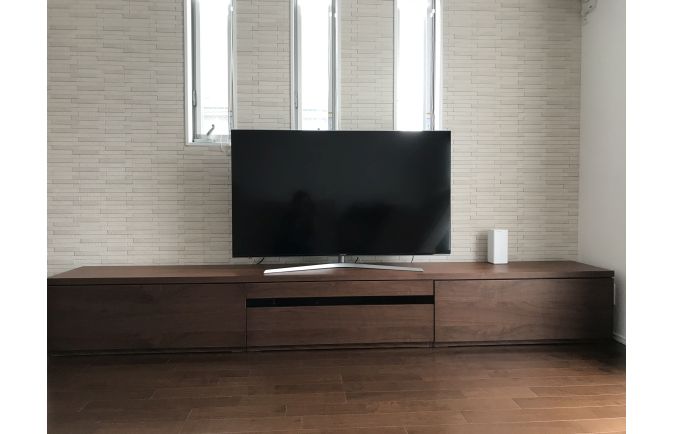 オシャレな明り取りの窓とタイル調の壁面に設置された大川家具の無垢テレビボード(ルームズ大正堂)